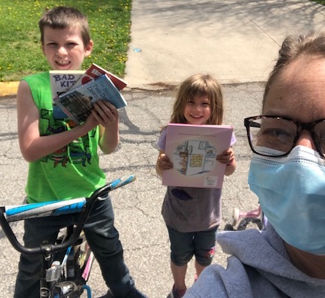 Two kids and a masked adult with books from CIS.